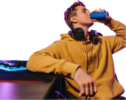 Portrait of young professional cyber sportsman sitting at gaming desk at home and drinking caffeine energy drink to concentrate on online video shooter game at night. Neon coloured room. Cyber sport