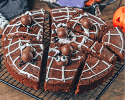 Chocolate cobweb brownies with candy spiders, homemade treats for Halloween on rustic wooden background. Selective focus