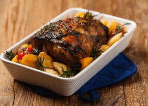 Roasted whole shoulder, with potatoes, peppers and tomatoes. Marinated in white wine. Front view. Natural wooden background. 