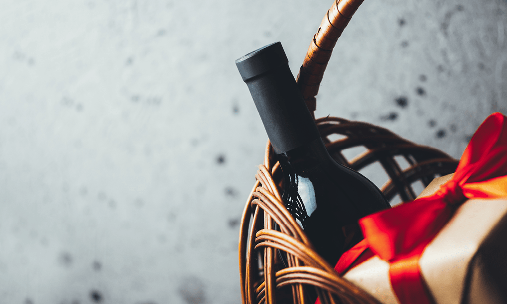 A bottle of wine is in a basket with a red bow. Description generated by AI