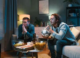 Two men sitting on a couch watching TV. Description generated by AI