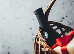 A bottle of wine is in a basket with a red bow. Description generated by AI