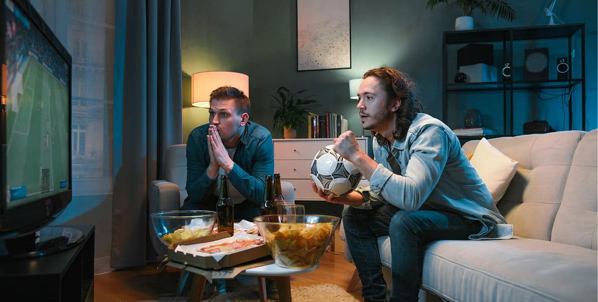 Two men sitting on a couch watching television. Description generated by AI