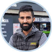 A man with a beard and a gray vest is standing in front of a store. Description generated by AI