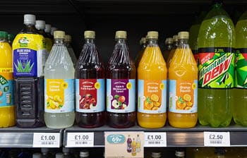 Bottles of various flavored squash drinks and Mountain Dew are displayed on a supermarket shelf with price labels below. Description generated by AI