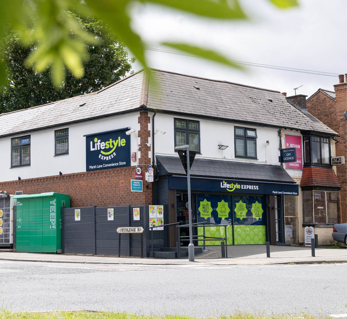 A corner convenience store named Lifestyle Express with a brick and white exterior is situated on a street with visible signage and a green utility box nearby. Description generated by AI