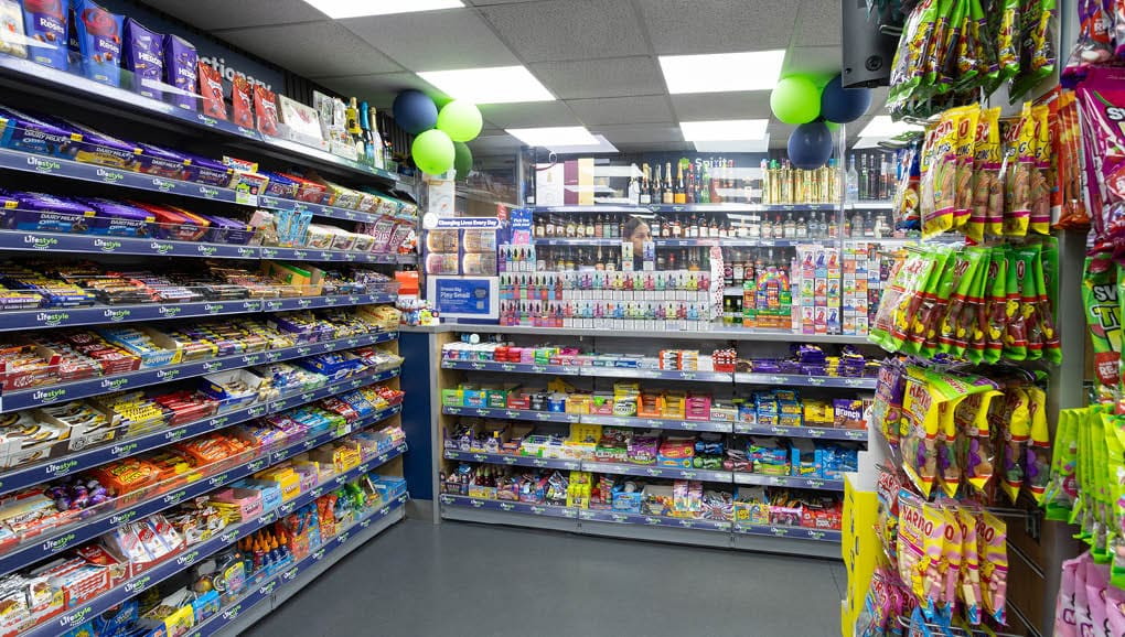 A brightly lit convenience store aisle filled with various colorful packaged snacks and candies on shelves and hanging displays. Description generated by AI