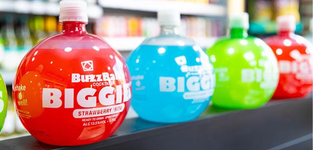 A row of colorful round bottles labeled “BuzzBallz" with different flavors is displayed on a shelf in a store. Description generated by AI