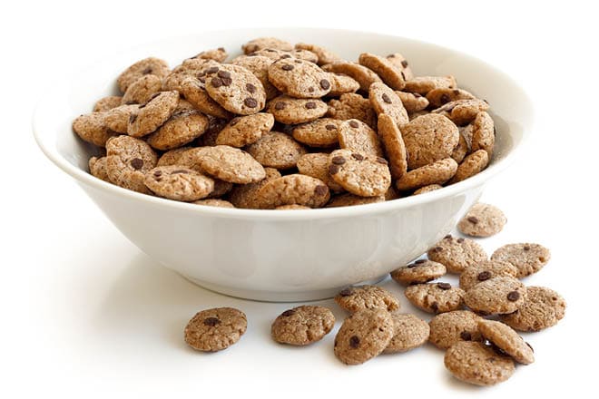 Bowl of chocolate chip cookies cereal isolated on white. Spilled cookies.