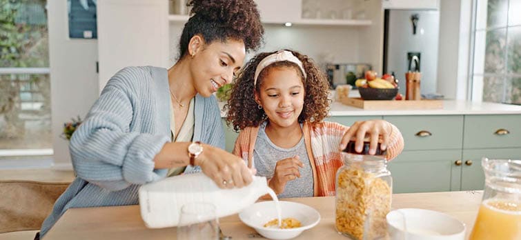 Mother, child and breakfast cereal in morning for healthy nutrition with calcium milk, preparing or home. Woman, daughter and growth development in kitchen for wellness fiber or snack, hungry or food.