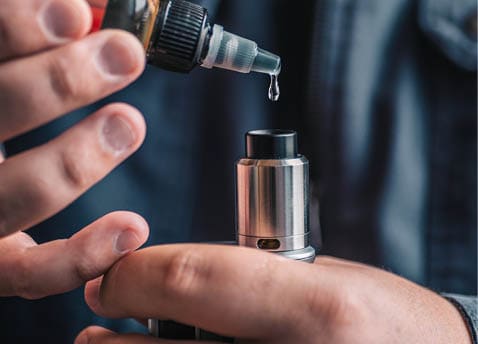 A person is holding a vaping device while carefully dripping e-liquid from a small bottle onto the device. Description generated by AI