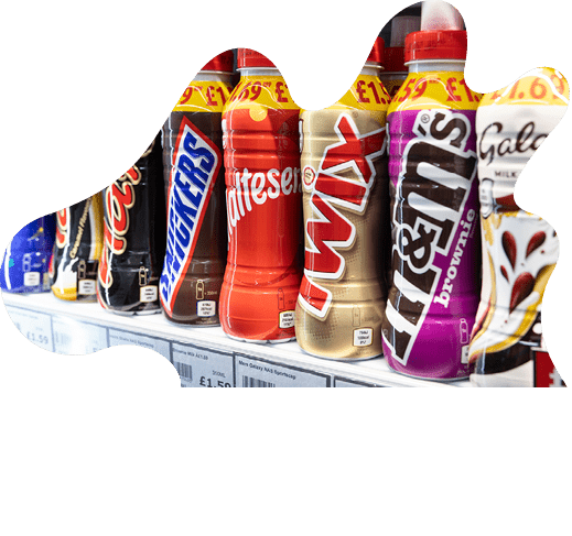 A row of chocolate-flavored milk bottles designed to look like popular candy bars is displayed on a store shelf with price tags visible. Description generated by AI