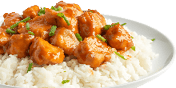 Chunks of chicken coated in a glossy orange sauce are served on a bed of white rice garnished with chopped green herbs on a white plate. Description generated by AI