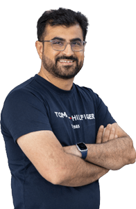 A person with short dark hair and glasses is smiling with arms crossed, wearing a navy blue Tommy Hilfiger t-shirt and a smartwatch with a blue band. Description generated by AI