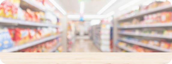 A wooden surface in the foreground with blurred shelves of various products in a brightly lit store aisle in the background. Description generated by AI