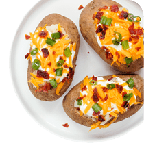 Three baked potatoes topped with sour cream, shredded cheddar cheese, chopped green onions, and bacon bits on a white plate. Description generated by AI